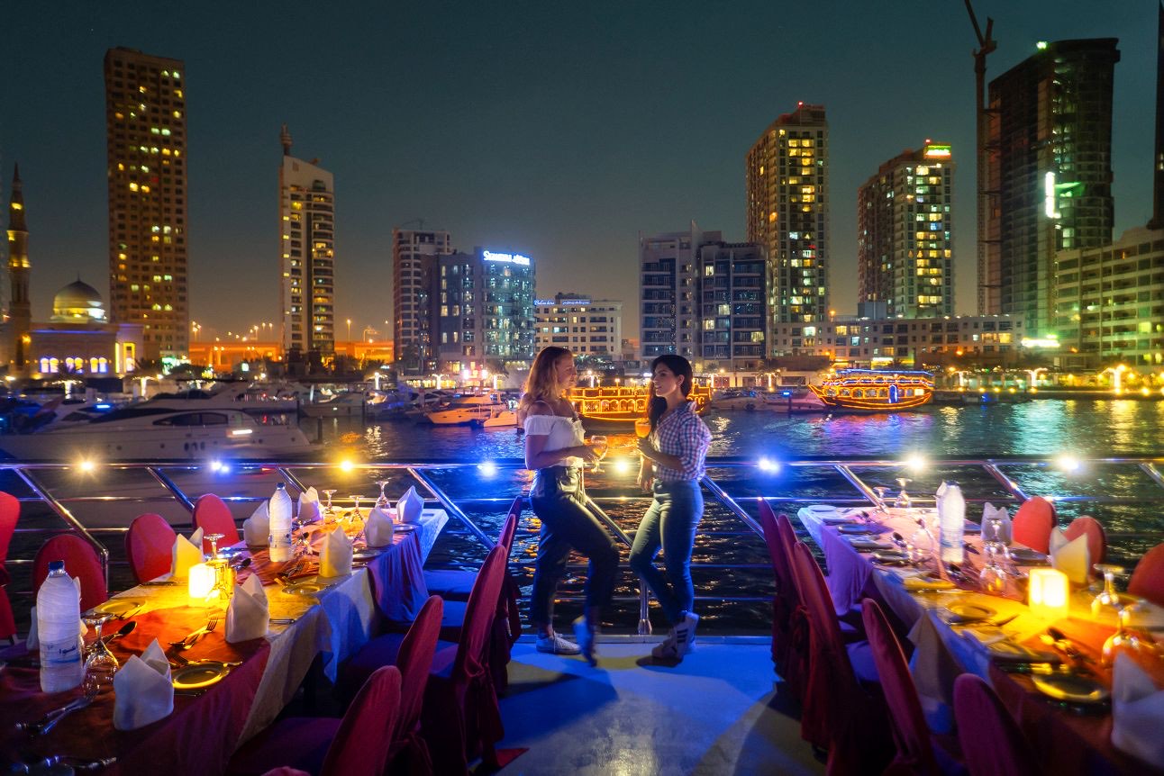Guests on the open upper deck with the marina lit behind them